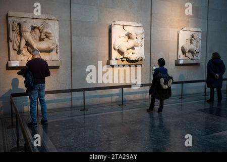 Les visiteurs du British Museum de Londres admirent les métopes du Parthénon grec ancien, également connues sous le nom de marbres du Parthénon (Elgin), le 28 novembre 2023, à Londres, en Angleterre. Quatre-vingt-douze métopes étaient des dalles de marbre rectangulaires placées sur les colonnes du temple du Parthénon d'Athènes représentant des scènes de la mythologie grecque. Banque D'Images