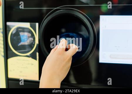 Distributeur automatique de recyclage pour distribuer de l'argent liquide. La main de l'homme met la bouteille en plastique à la machine Banque D'Images