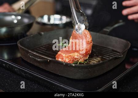 Gros plan du morceau de viande crue placé sur le gril avec des pinces métalliques Banque D'Images