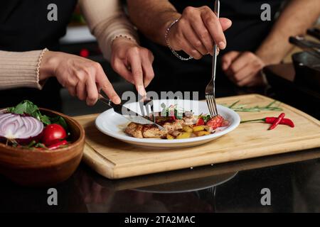Gros plan des mains d'un homme méconnaissable et d'une femme mangeant du steak et des légumes d'une assiette coupant la nourriture en morceaux Banque D'Images