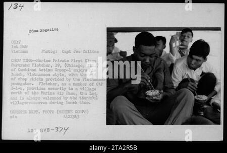 Légende : Marine Private First Class Bertrand Fletcher, du Combined action Group-1, prend un repas à l'aide de baguettes fournies par un enfant vietnamien à l'heure du déjeuner. Fletcher, qui sert dans CAP 1-1-4, assure la sécurité d'un village au nord de la base aérienne de Chu Lei, et est chaleureusement accueilli par des villageois reconnaissants. Cette photographie a été prise en 1968 par le capitaine Joe Collins, membre du corps des Marines des États-Unis. Banque D'Images