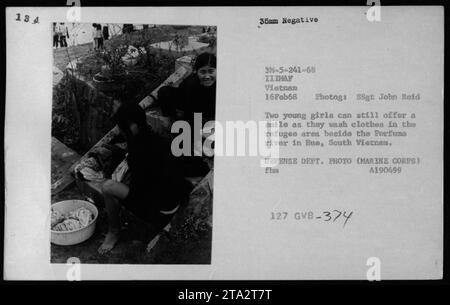 Deux jeunes filles lavent leurs vêtements dans la zone des réfugiés près de la rivière des parfums à Hue, au Sud-Vietnam, le 16 février 1968. Malgré les circonstances difficiles, ils parviennent toujours à offrir un sourire. Cette photographie a été prise par le Sgt John Reid et fait partie des archives de la guerre du Vietnam. Banque D'Images