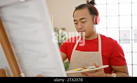 Jeune homme chinois sérieux avec coiffure de queue de cochon, artiste debout dans le studio d'art universitaire, maîtrisant sans effort l'art de dessiner tout en intensément l Banque D'Images