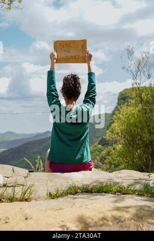 Vue arrière d'une femme tenant un papier avec un message écologique pour sauver la planète avec un ciel Banque D'Images