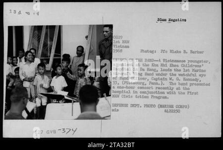 Civil vietnamien à l'hôpital pour enfants Khu Nhi Khoa à Da Nang dirigeant le 1st Marine Aircraft Wing Band lors d'un concert. Officier de bande, capitaine W. G. Kennedy, 33 ans, supervisant la performance. Le concert faisait partie du First HAW Civic action Program. Prise en 1968 dans le cadre de la guerre du Vietnam. Banque D'Images