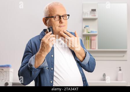 Homme mature utilisant une machine à raser dans une salle de bain Banque D'Images