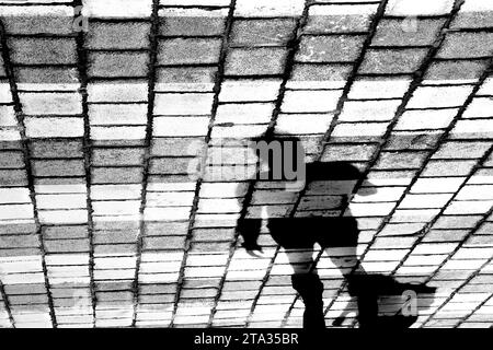 Silhouette d'ombre d'une personne traversant la rue en galets sur le croisement de pélicans, en noir et blanc Banque D'Images