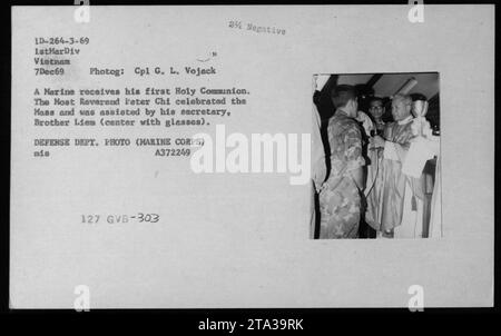 'Le personnel militaire assistant à une cérémonie religieuse pendant la guerre du Vietnam. Un Marine reçoit sa première communion tandis que le très révérend Peter Chi officie la messe. Frère Liem, le secrétaire du révérend, peut être vu l'assister au centre de l'image. Photographie prise par le Cpl G. L. Vojack, USMC, le 7 décembre 1969.' Banque D'Images