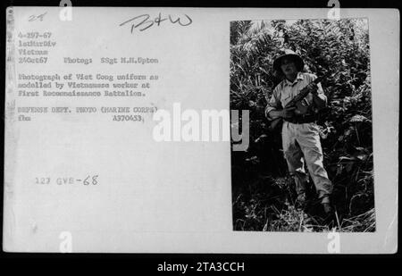 Photographie représentant un ouvrier vietnamien modélisant un uniforme Viet Cong au premier bataillon de reconnaissance pendant la guerre du Vietnam. L'image montre des armes capturées et a été prise le 24 octobre 1967 par le SSgt M.M. Upton, un photographe de la 1e Division des Marines au Vietnam. La photographie est une photo officielle du ministère de la Défense. Banque D'Images