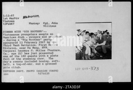 Des jeunes Vietnamiens participent à un groupe de « Big Brother » parrainé par le troisième bataillon de chars, première division des Marines, près de Da Nang, RVN, le 12 février 1967. Le caporal Leonere J. Stiles présente à l'un des 150 invités une assiette de seineuses et de choucroute. L'événement comprenait également de la boxe, du softball, un remorqueur de guerre et une montée de poteau graissée. Banque D'Images