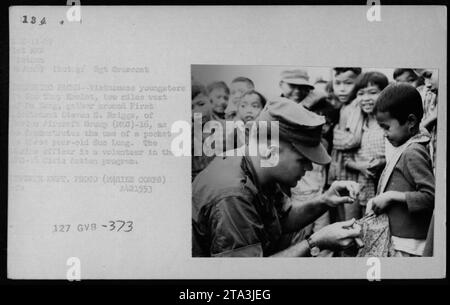 Des enfants vietnamiens dans le hameau de son Thuy près de Da Lang, se rassemblent autour du premier lieutenant Steven S. Briggs du groupe Aircroft (a)-16, alors qu'il démontre l'utilisation d'une poche à une jeune fille nommée Sue long. Le lieutenant Briggs est bénévole dans le programme O-15 Civic action. Banque D'Images