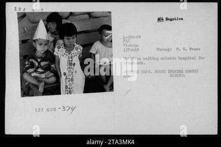 Enfants attendant devant un hôpital au Vietnam, 13 février 1968. Cette photographie, prise par P.D. Evans, capture une scène représentant la vie civile vietnamienne pendant la guerre du Vietnam. Les enfants attendent un traitement médical à l'hôpital. L'image fait partie de la collection de photos officielle du département de la Défense. Banque D'Images