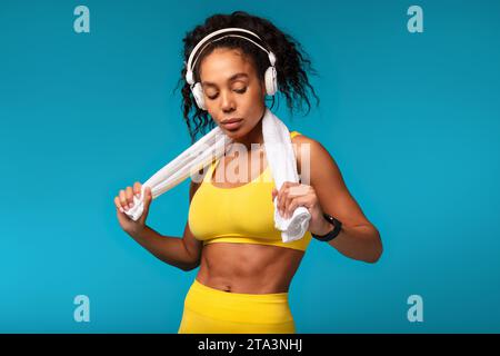 Black Fitness Lady portant casque sans fil debout avec serviette, Studio Banque D'Images