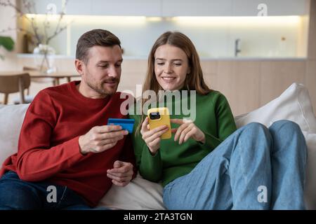 Couple de famille agréable faisant des achats payer des achats en ligne dans le téléphone portable, réserver des billets d'avion. Banque D'Images