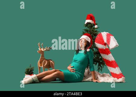 Femme afro-américaine enceinte dans le chapeau de Santa avec décor de Noël sur fond vert Banque D'Images