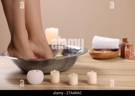 Femme trempant ses pieds dans un bol avec de l'eau et des fleurs sur la surface en bois, gros plan. Procédé de pédicure Banque D'Images