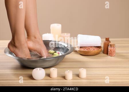 Femme trempant ses pieds dans un bol avec de l'eau et des fleurs sur la surface en bois, gros plan. Procédé de pédicure Banque D'Images