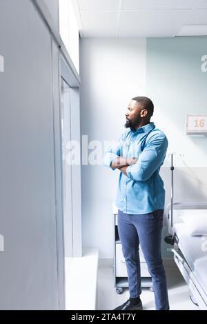 Médecin afro-américain réfléchi regardant par la fenêtre dans la chambre d'hôpital, espace de copie Banque D'Images