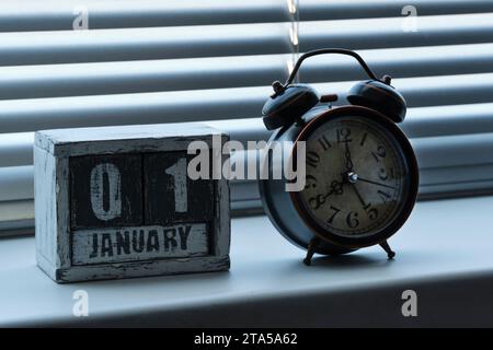 Matin du 01 janvier sur la fenêtre debout de calendrier en bois avec des stores à côté d'un réveil indiquant huit heures Banque D'Images