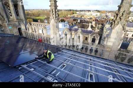 Un ingénieur photovoltaïque travaille à l'installation de 438 nouveaux panneaux solaires photovoltaïques sur le toit de la chapelle récemment restaurée du King's College Cambridge. Les panneaux répondront à 100 % des besoins énergétiques de la Chapelle et réduiront les émissions de carbone du Collège de plus de 27 tonnes par an. Date de la photo : mardi 28 novembre 2023. Banque D'Images