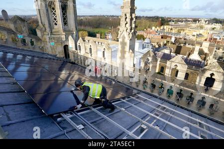 Un ingénieur photovoltaïque travaille à l'installation de 438 nouveaux panneaux solaires photovoltaïques sur le toit de la chapelle récemment restaurée du King's College Cambridge. Les panneaux répondront à 100 % des besoins énergétiques de la Chapelle et réduiront les émissions de carbone du Collège de plus de 27 tonnes par an. Date de la photo : mardi 28 novembre 2023. Banque D'Images