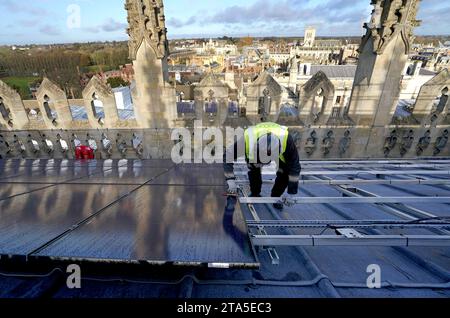 Un ingénieur photovoltaïque travaille à l'installation de 438 nouveaux panneaux solaires photovoltaïques sur le toit de la chapelle récemment restaurée du King's College Cambridge. Les panneaux répondront à 100 % des besoins énergétiques de la Chapelle et réduiront les émissions de carbone du Collège de plus de 27 tonnes par an. Date de la photo : mardi 28 novembre 2023. Banque D'Images