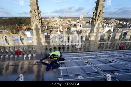 Un ingénieur photovoltaïque travaille à l'installation de 438 nouveaux panneaux solaires photovoltaïques sur le toit de la chapelle récemment restaurée du King's College Cambridge. Les panneaux répondront à 100 % des besoins énergétiques de la Chapelle et réduiront les émissions de carbone du Collège de plus de 27 tonnes par an. Date de la photo : mardi 28 novembre 2023. Banque D'Images