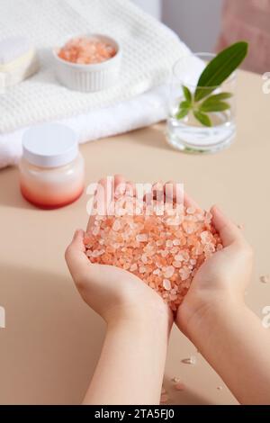 Un tas de sel rose de l'himalaya entre les mains. Pot cosmétique sans étiquette affichée. Le sel rose de l'himalaya peut améliorer les conditions de la peau et apaiser les douleurs musc Banque D'Images