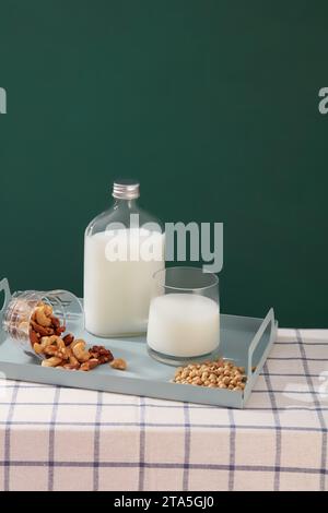 Bouteille de lait sans étiquette affichée sur un plateau avec une tasse de lait et différents types de haricots et de noix. Modèle pour modéliser votre conception de pro organique Banque D'Images