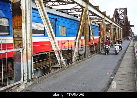 Les motocyclistes montent à côté d'un train à grande vitesse sur le pont long bien à Hanoi, Vietnam. Le pont a été bombardé à plusieurs reprises pendant la guerre du Vietnam Banque D'Images