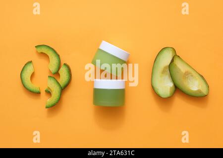 Maquette de produit de beauté, pots cosmétiques décorés de tranches fraîches d'avocat sur fond orange. Vue de dessus, scène pour la publicité et le cosmet de marque Banque D'Images