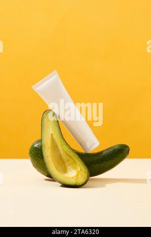 Vue de face de la bouteille en plastique blanc placé sur l'avocat frais et la tranche d'avocat sur fond jaune. Produits de soins de la peau à base d'avocat naturels pour une peau saine Banque D'Images