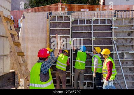 Vue de derrière sur le travailleur comme spectacles chantent avec la main à la grue comme équipe de travailleurs de la construction avec gilet de sécurité et casques jaunes assemblage manuel haut Banque D'Images