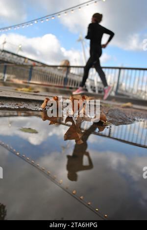 Un joggeur court devant une flaque d'eau d'automne sur Londres Southbank. Banque D'Images