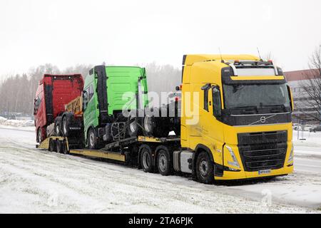 Camion porteur de véhicules Volvo FH jaune transportant deux nouveaux camions Volvo verts et rouges garés dans les chutes de neige hivernales. Salo, Finlande. 24 novembre 2023. Banque D'Images