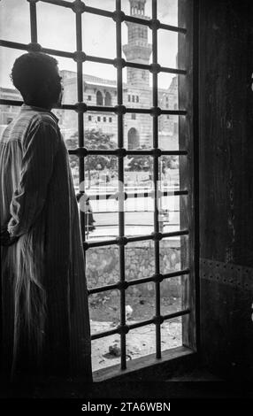 Un jeune homme regarde par une fenêtre dans la Citadelle du Caire en Egypte dans les années 1930, il regarde vers la mosquée Sultan Hassan Banque D'Images