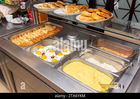 Fast food bistro, nourriture dans des plateaux en métal, salade de côtelettes garniture sur la fenêtre du café, patches avec nourriture sur le comptoir de bistro, viande et garniture dans des patches. Banque D'Images