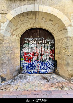Vieilles portes en chêne dans une élégante entrée en arche altérée par le marquage et la pulvérisation de graffiti - Tours, Indre-et-Loire (37), France. Banque D'Images