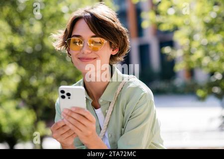 Photo de belle fille joyeuse habillée chemise élégante lisant le télégramme instagram passer du temps libre se détendre reste vert parc à l'extérieur Banque D'Images