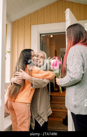 Joyeuse femme âgée accueillant fille et petite-fille à la maison Banque D'Images