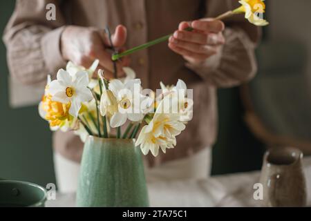 Gros plan d'une femme arrangeant un bouquet de jonquilles dans un vase Banque D'Images