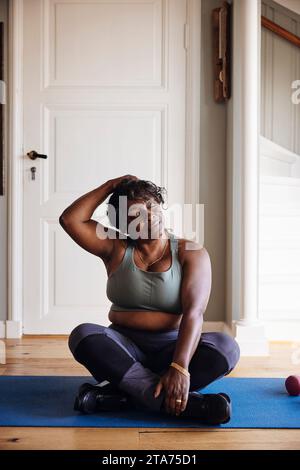 Femme mature avec les yeux fermés pratiquant l'exercice de relaxation sur tapis à la maison Banque D'Images