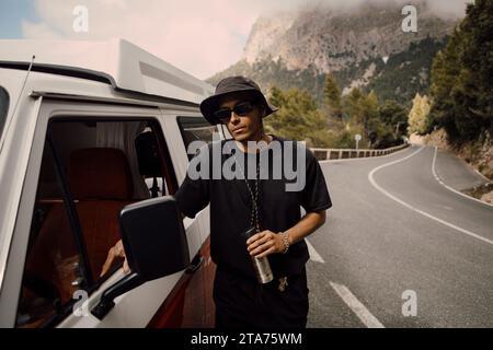 Jeune homme portant des lunettes de soleil debout à côté de la camionnette pendant le voyage sur la route Banque D'Images