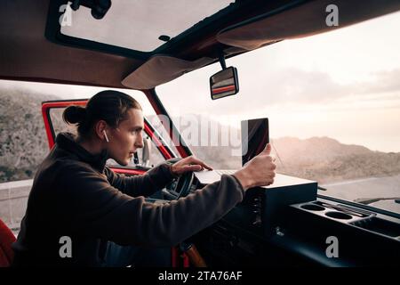 Vue latérale d'un homme avec des écouteurs intra-auriculaires sans fil utilisant un ordinateur portable assis dans une camionnette en vacances Banque D'Images