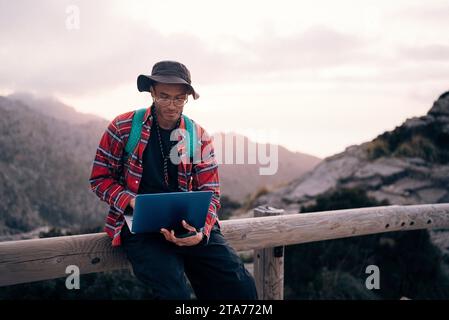 Jeune homme utilisant un ordinateur portable assis sur la rampe au coucher du soleil Banque D'Images
