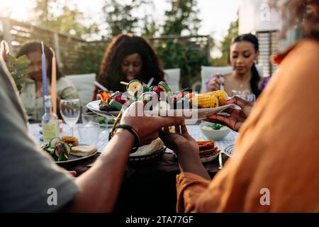 Amis passant une assiette de collations à l'autre pendant le dîner dans la cour arrière Banque D'Images