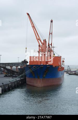 Un vraquier avec des grues rouges distinctives est amarré sur les quais de Walvis Bay, sous un ciel couvert Banque D'Images