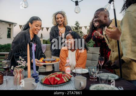 Femme surprenante amie féminine avec gâteau lors de la célébration d'anniversaire dans la cour arrière Banque D'Images