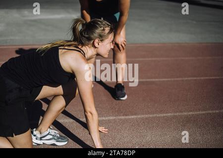 Vue latérale de la jeune femme se préparant au sprint sur piste de course Banque D'Images