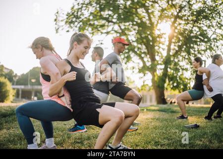 Souriant multiracial hommes et femmes amis faisant copain dos étirer sur l'herbe au parc Banque D'Images